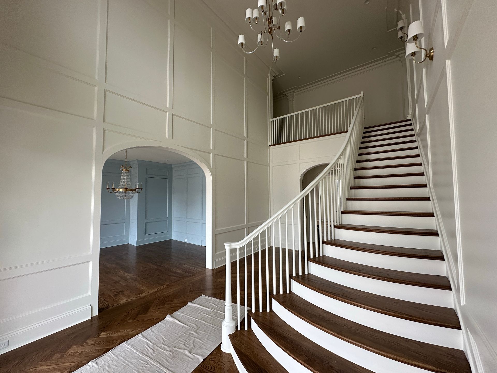 Elegant white paneled entryway with a winding staircase and chandelier.
