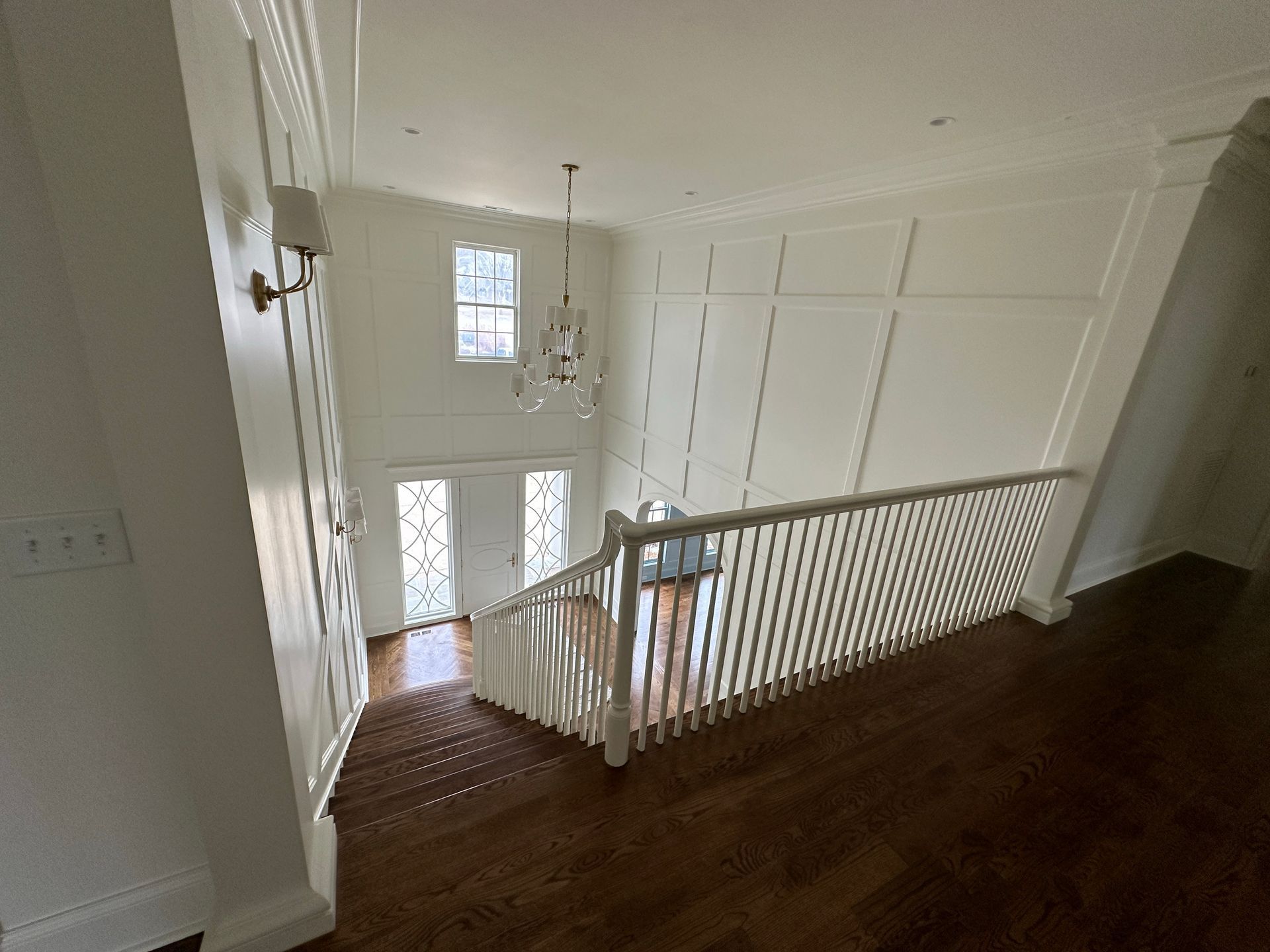 Interior view of a two-story foyer with white walls, dark wood floors, and a staircase.