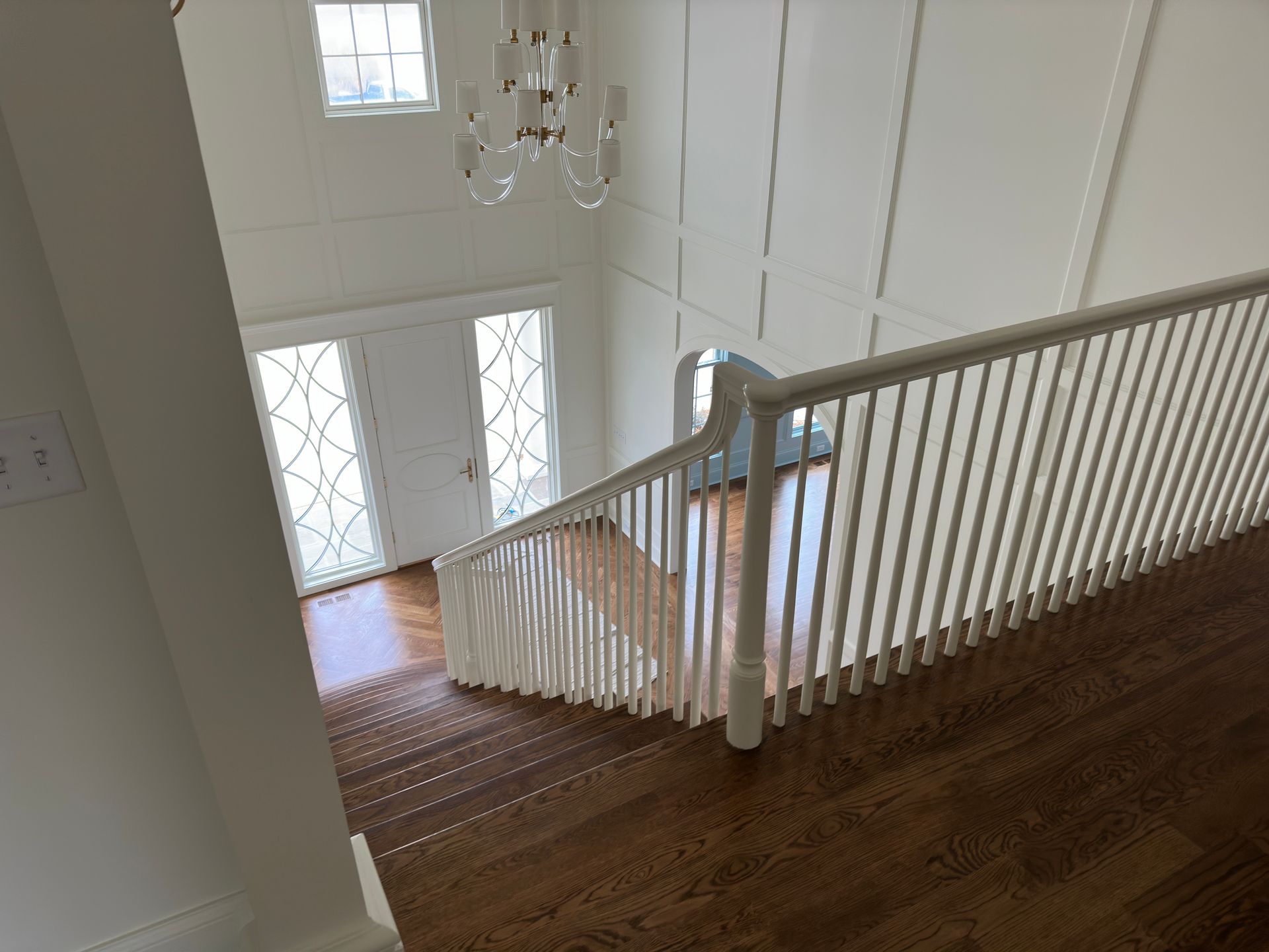Staircase with white railing and dark wood steps leads down to a bright entryway with double doors.