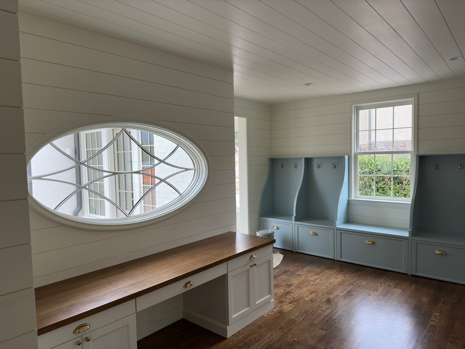 Interior room with built-in desk, oval window, blue lockers, and wooden floor.