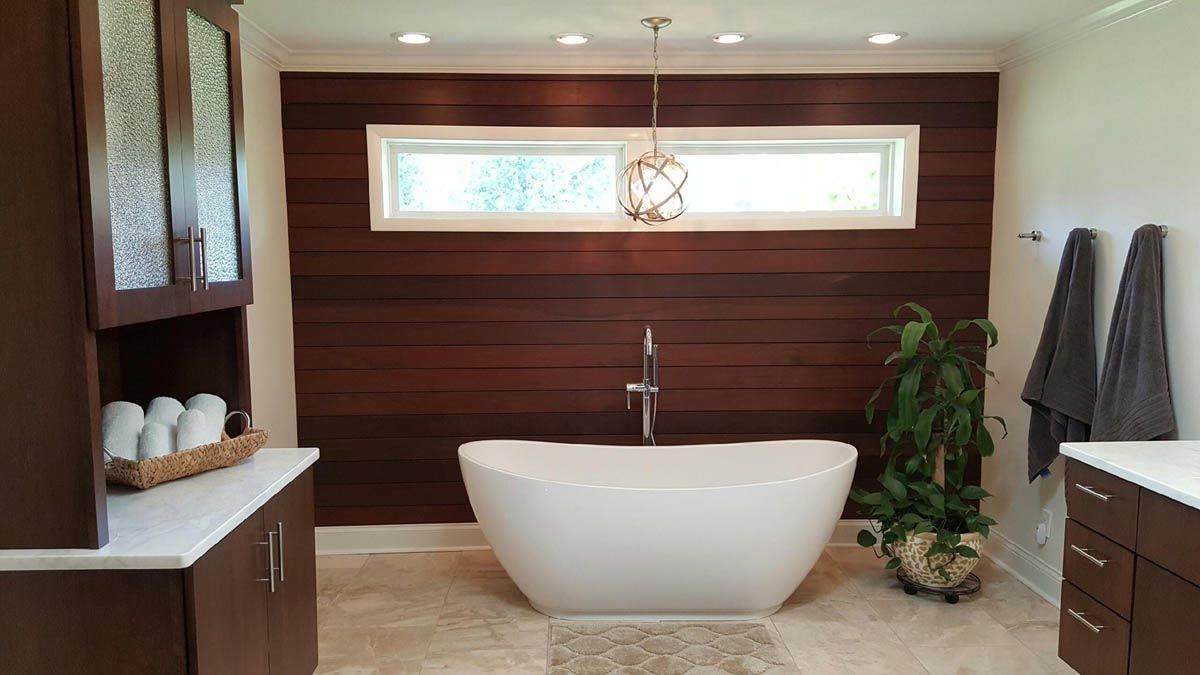 Modern bathroom with a white tub, dark wood accent wall, and cabinetry.