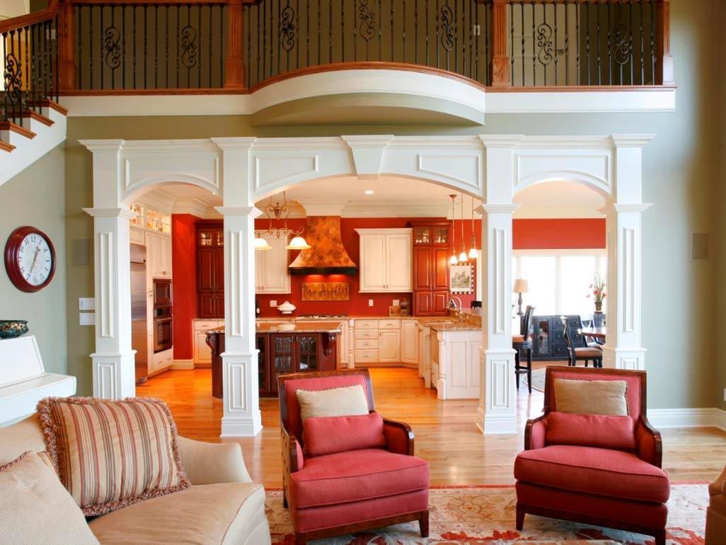 Living room with red chairs, a view of a kitchen, and a balcony above.