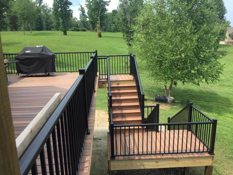 Wide angle view of a backyard with a new deck that is light brown with black iron rails.