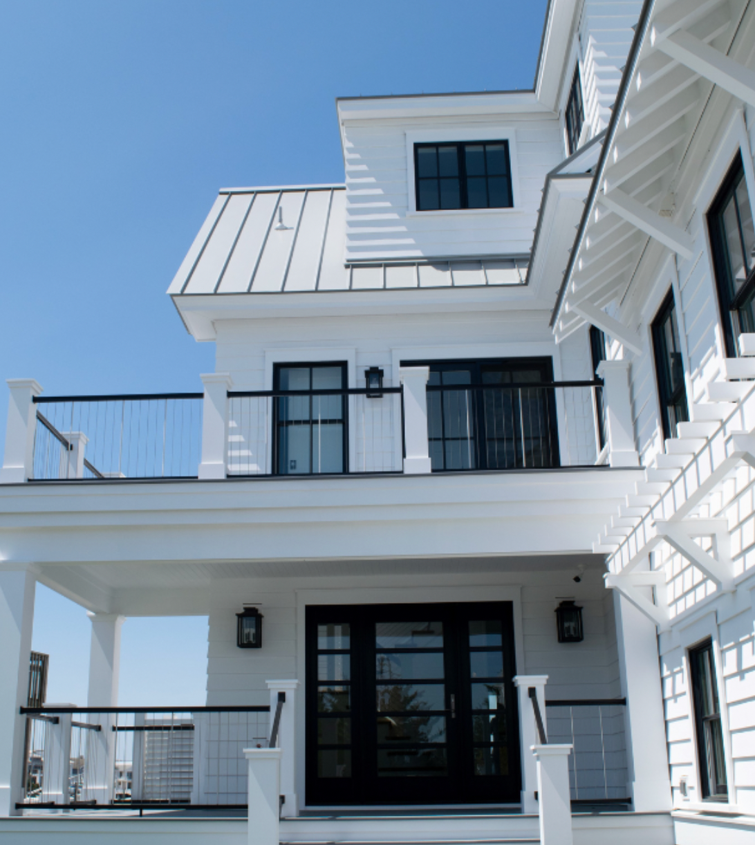 White house with black trim, a balcony, and a bright blue sky.