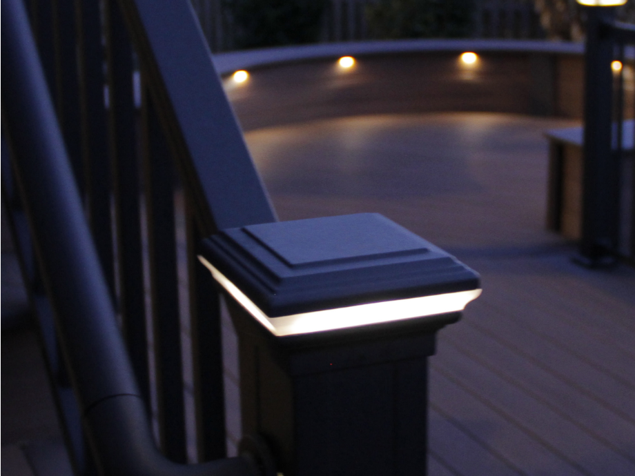Black deck railing post with integrated white LED light, deck boards in background.