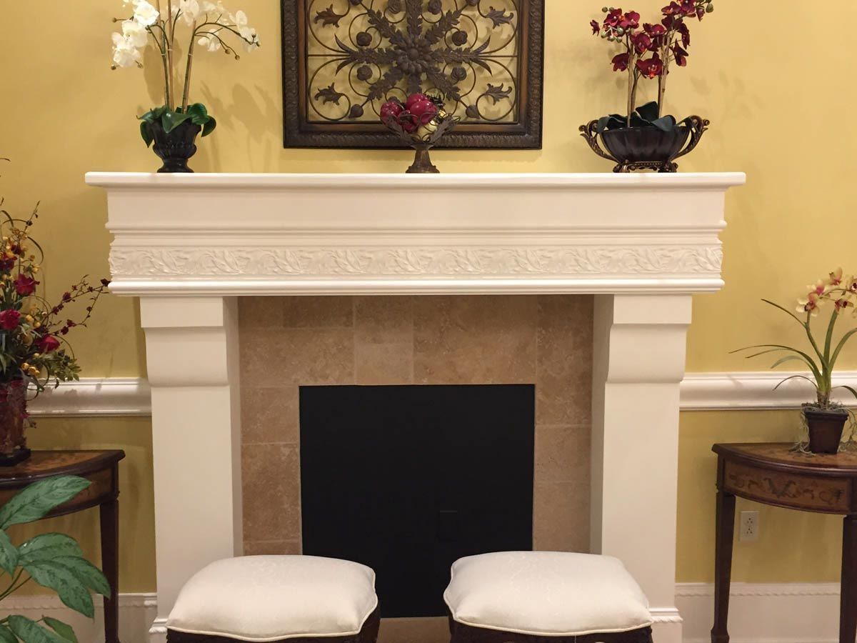 Fireplace with floral arrangements, artwork, and two small stools in front of it. Yellow walls.