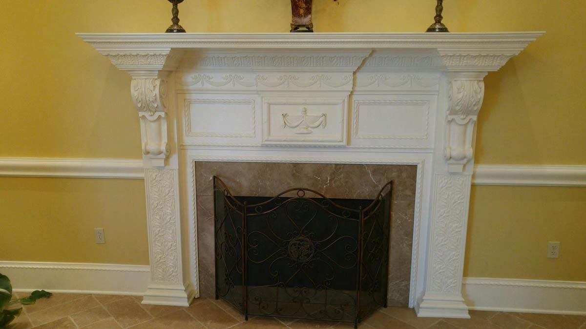 White fireplace with marble facing, a decorative screen, and candles on the mantle. Yellow walls.