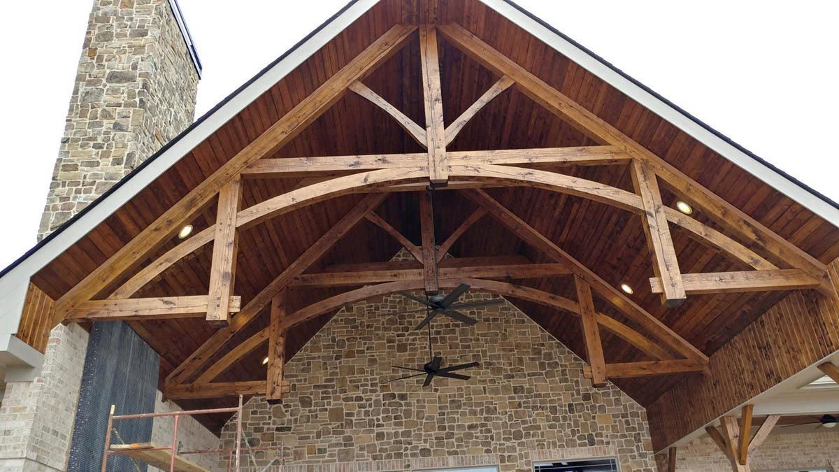 Wooden timber frame porch with arched beam over stone wall, two ceiling fans.