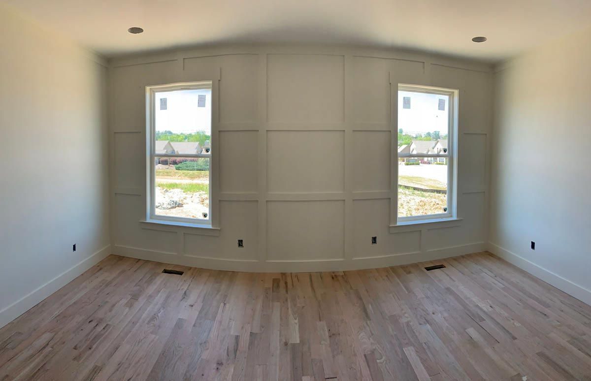 Empty room with hardwood floors, white walls, two windows, and paneled accent wall.