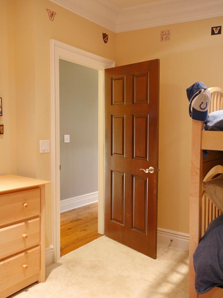 Ajar brown wooden door in a room with a beige wall, a dresser, and a bed.