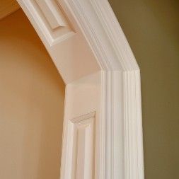 Close-up of white wooden door frame with detailed molding against light tan and olive walls.