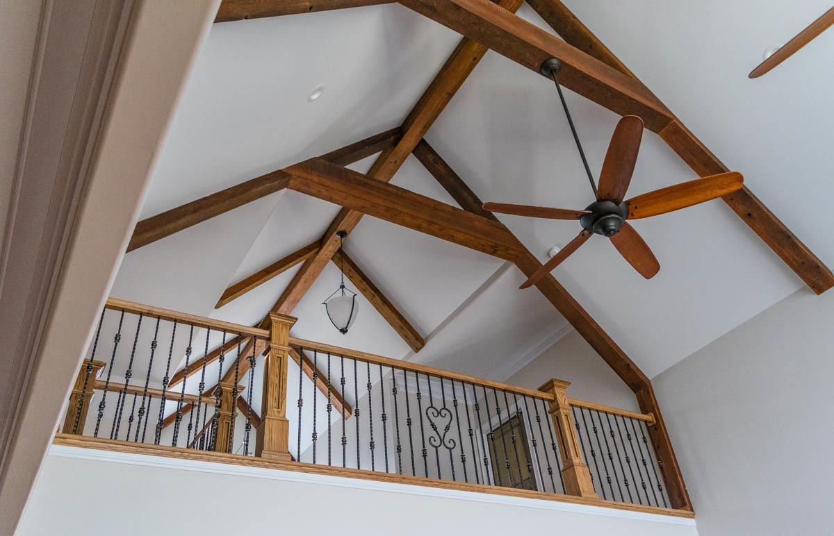 High ceiling with wooden beams, a ceiling fan, and a balcony with wrought iron railing.