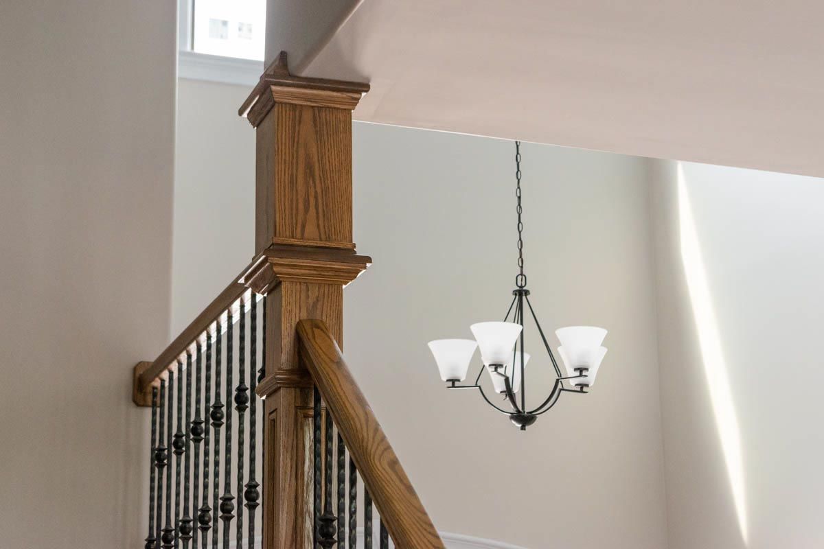 Wooden staircase with dark metal balusters, and a hanging chandelier.