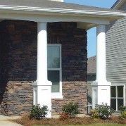 White columns on a house with brown stone and a window.