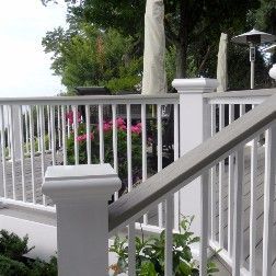 White and gray deck railing with vertical spindles, plants, and a partial view of a patio.