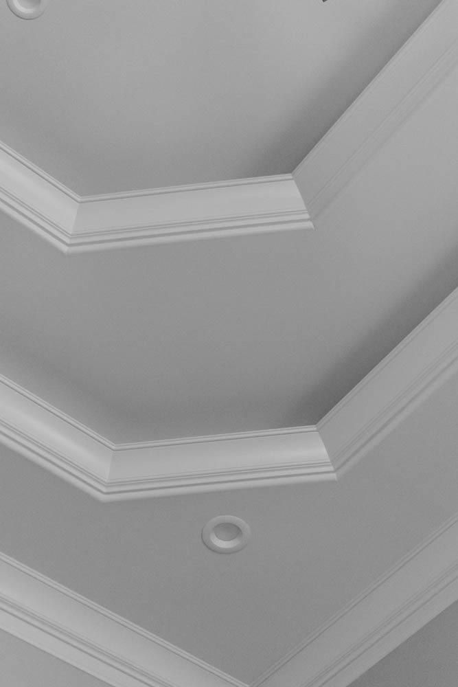 Angled white ceiling with layered crown molding and recessed lighting.