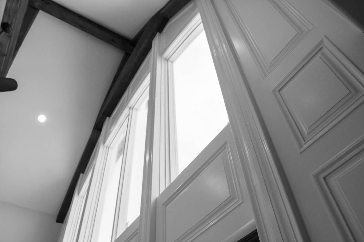 Interior view of tall windows with white paneling and dark wooden beams.