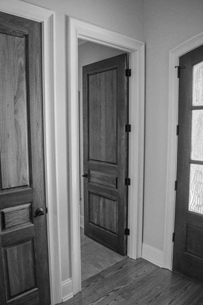 Three wooden doors in a hallway. Center door is open, revealing a view into another room.