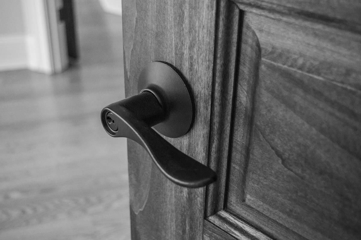 Black and white close-up of a door handle on a wooden door, partially open to reveal a room.