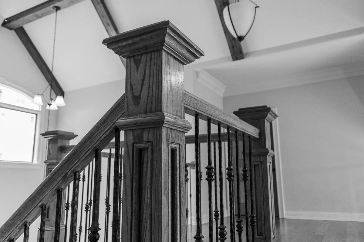 Black and white photo of a staircase with ornate wooden banister and railing, leading up to a light-filled space.