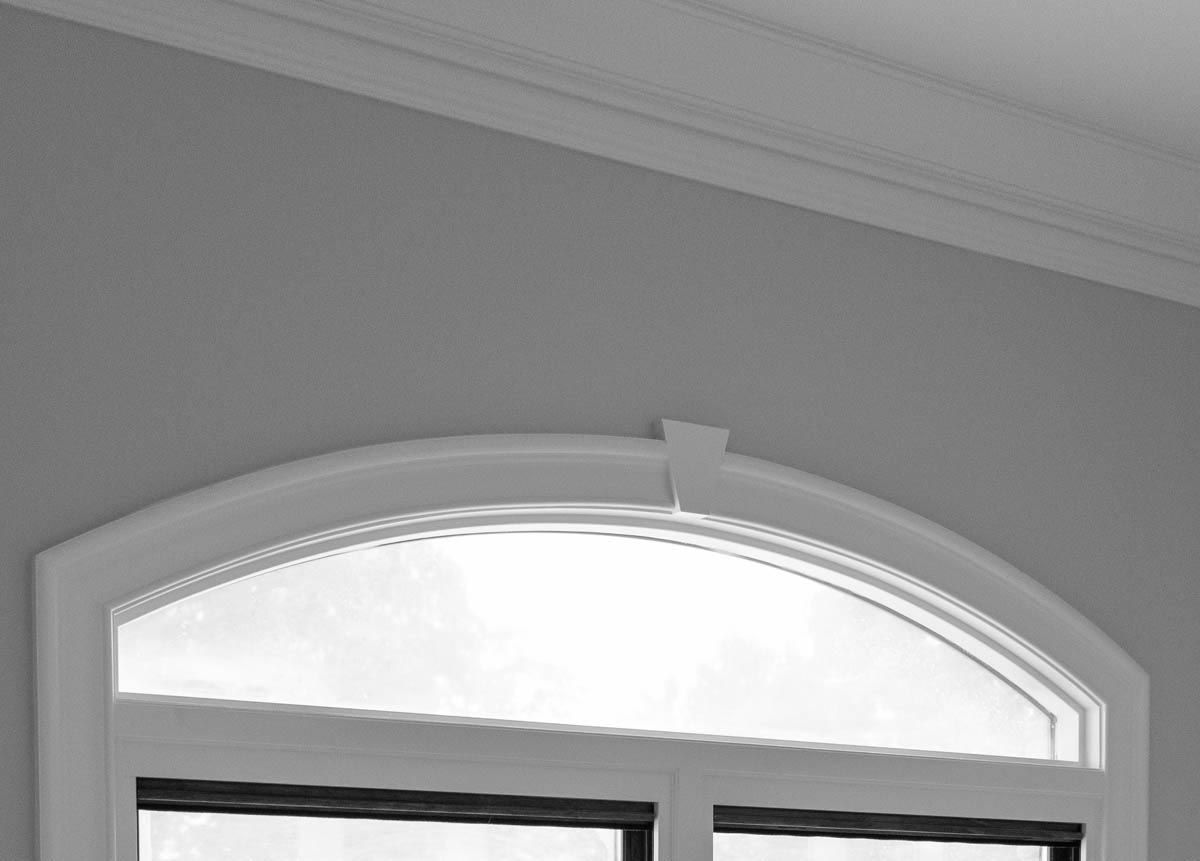Arched window with white trim, gray wall, and crown molding.