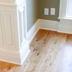 Corner of a room with hardwood floor, white molding, and light green walls.