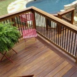 Wooden deck with railings, red chair, potted plant, and pool in the background.