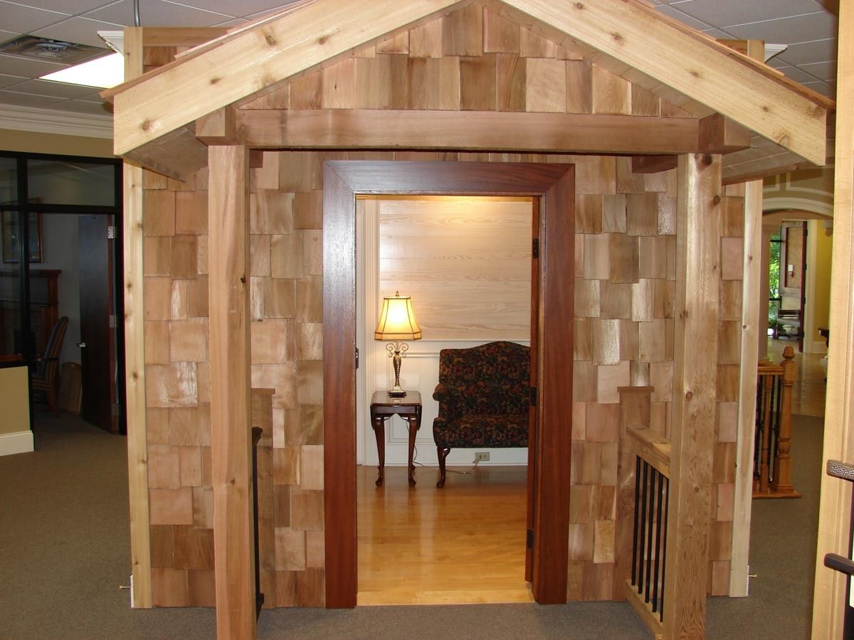 Wooden house facade with a door, leading to a room with a chair and lamp.