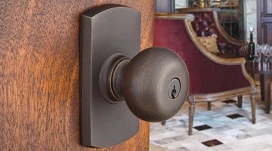 Bronze doorknob on wooden door, partially open. Interior with a red chair and wine glasses.