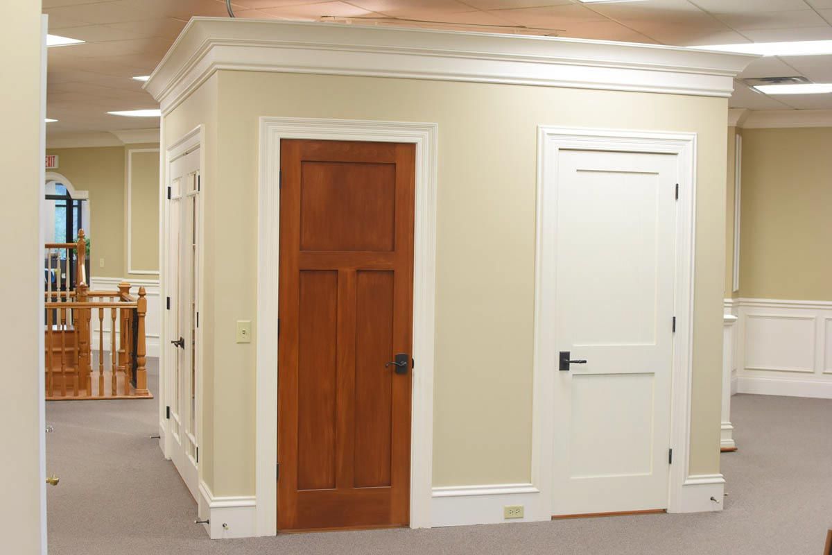 Three doors in a beige-walled room; a dark wooden door, a white door, and a partially visible door on the left.