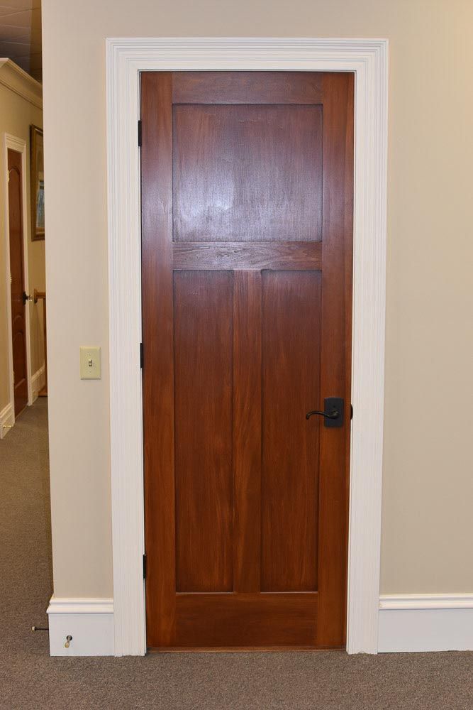Wooden door with dark stain, white trim, and a black handle.