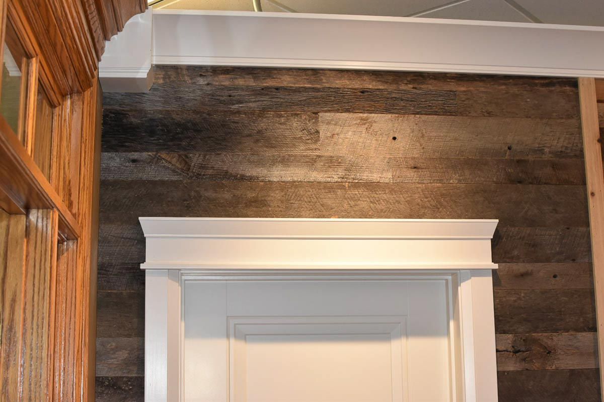 Wood-paneled wall with white door frame and trim; wood ceiling beam; natural light.
