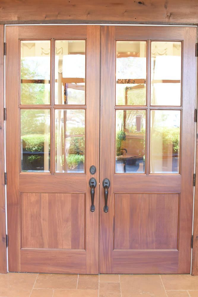 Wooden double doors with glass panes, black handles, and a glimpse of a sunlit interior.