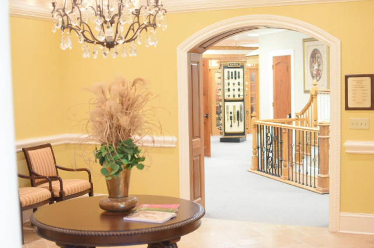 Yellow-walled entryway with round table, chairs, chandelier, and arched doorway to a showroom with doors.