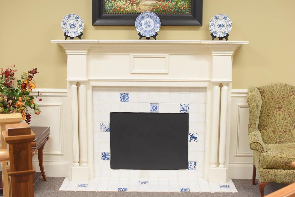 White fireplace with black insert, Delft-style tile, cream walls, and floral decor.