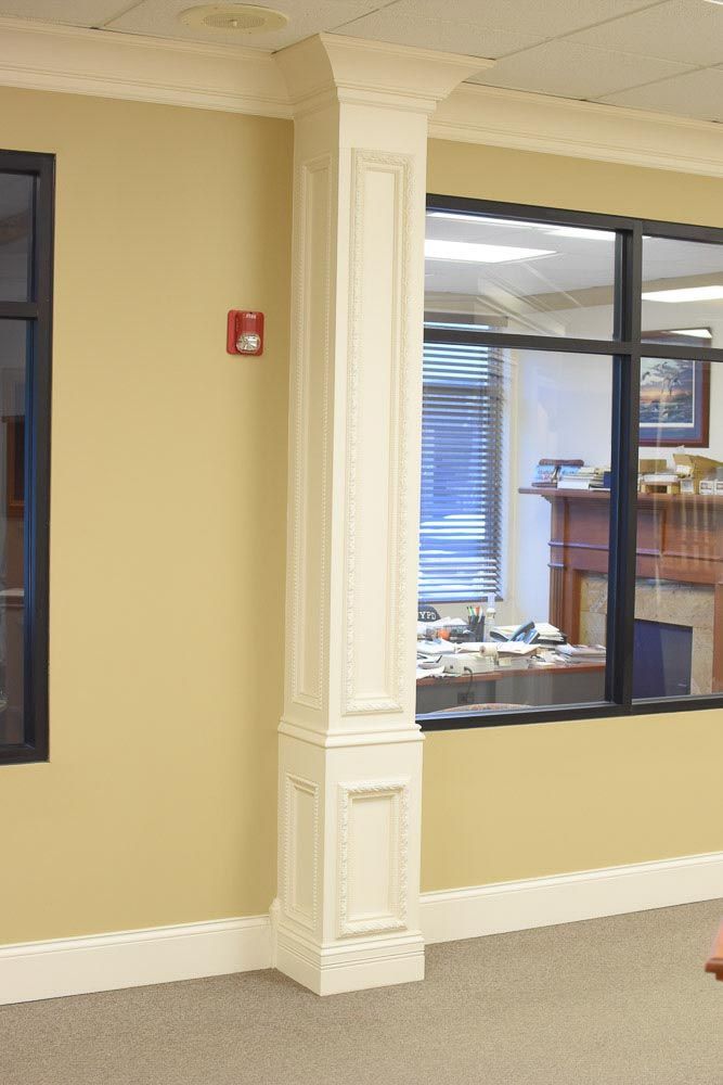 Cream-colored square column with decorative panels stands between windows and a wall.