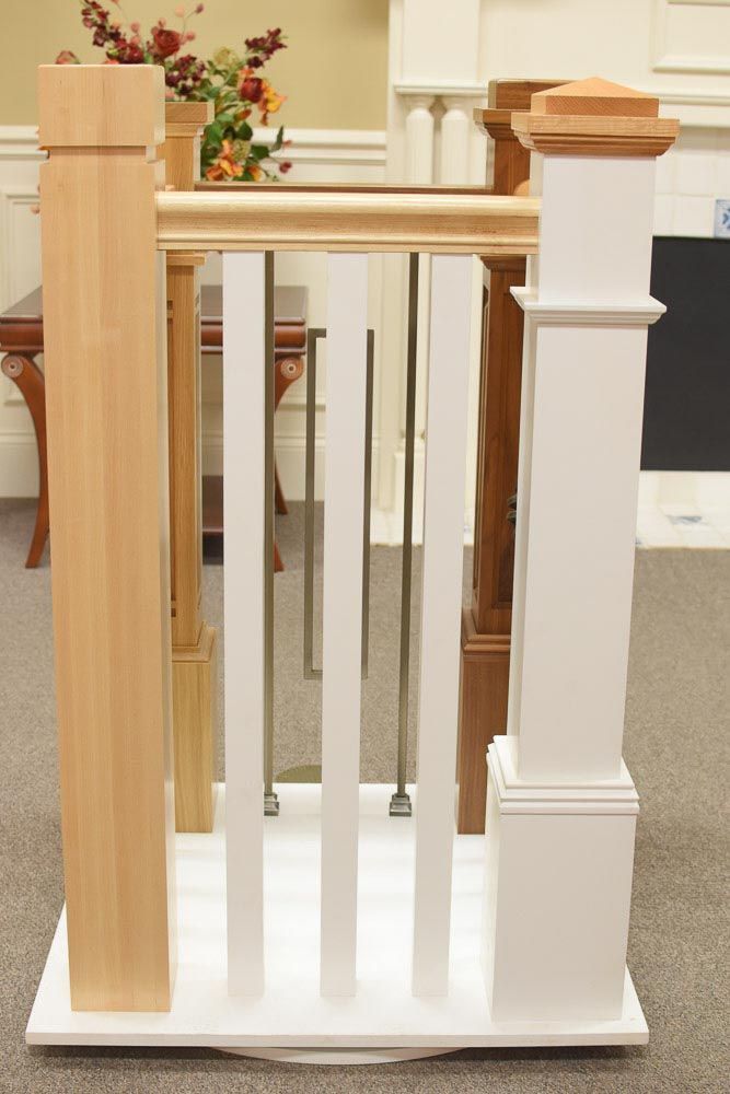 Staircase railing samples: various wooden and metal posts, white balusters, and floral arrangement in the background.