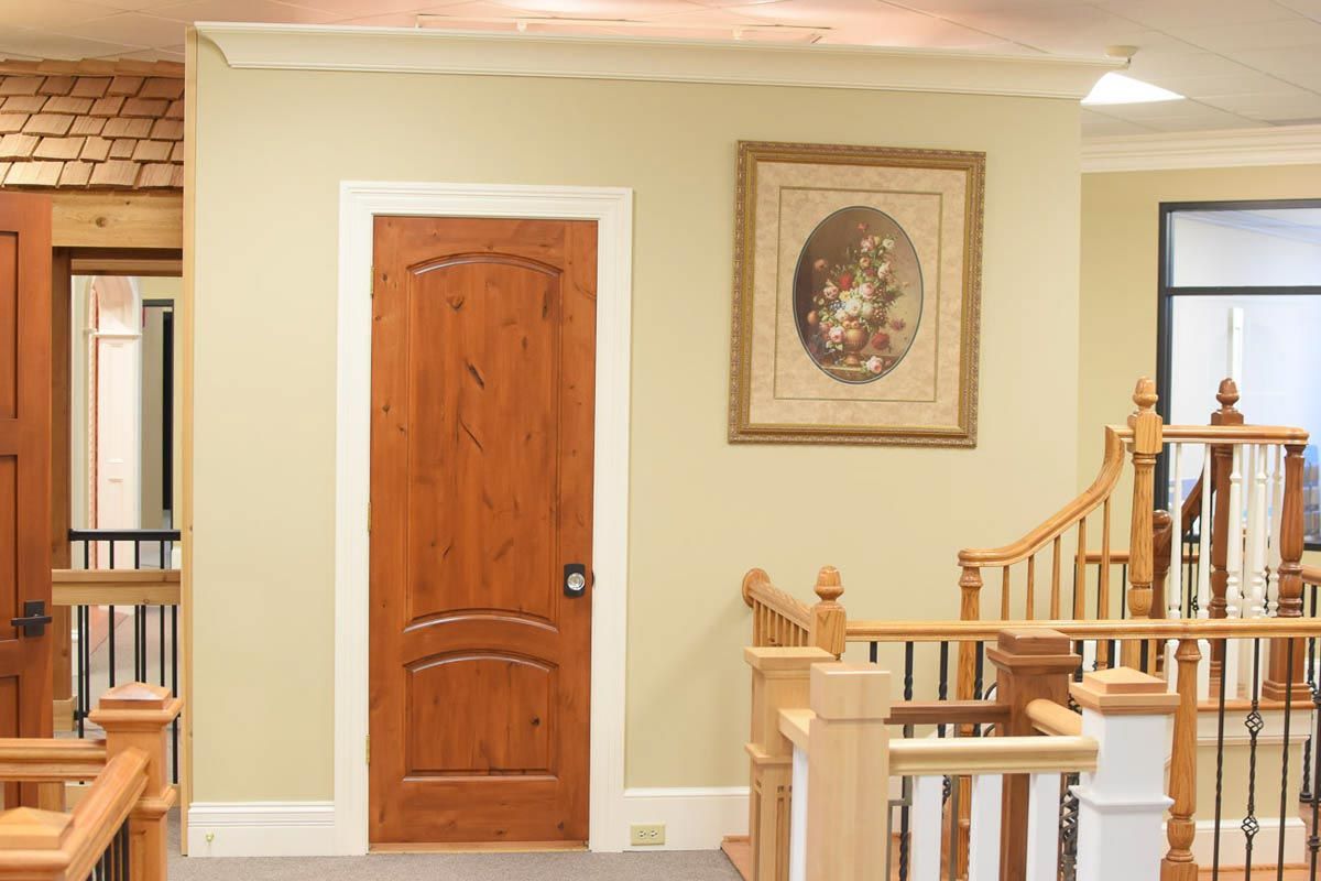 Wooden door and framed artwork on a beige wall, staircase with wooden railings in the foreground.