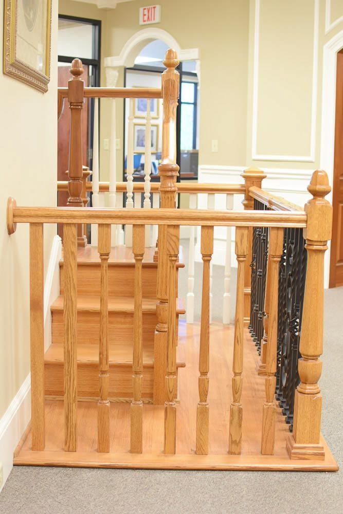Wooden staircase with railing and ornate balusters, leading up to a hallway.
