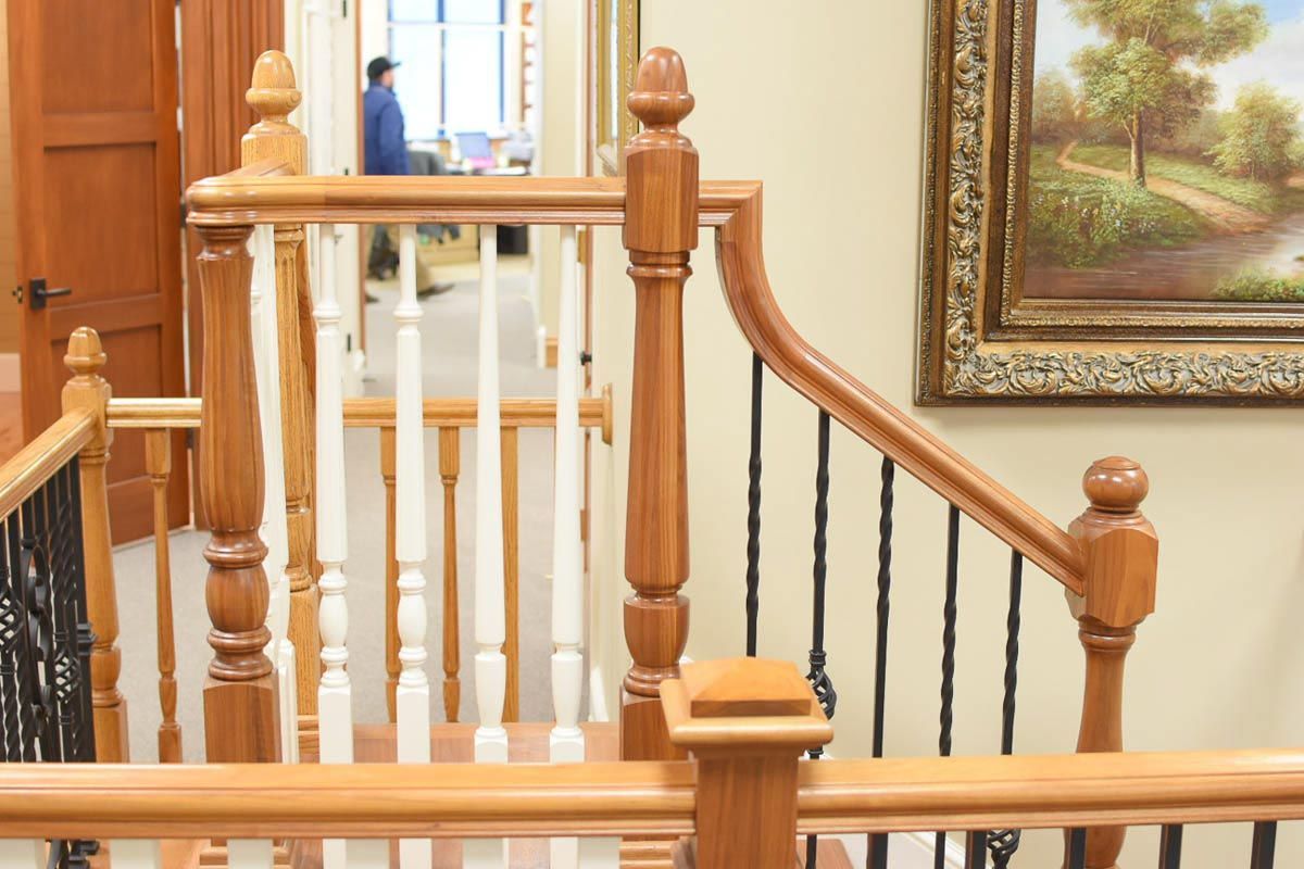 Wooden staircase with white and brown balusters, black wrought iron railing, and a painting on the wall.