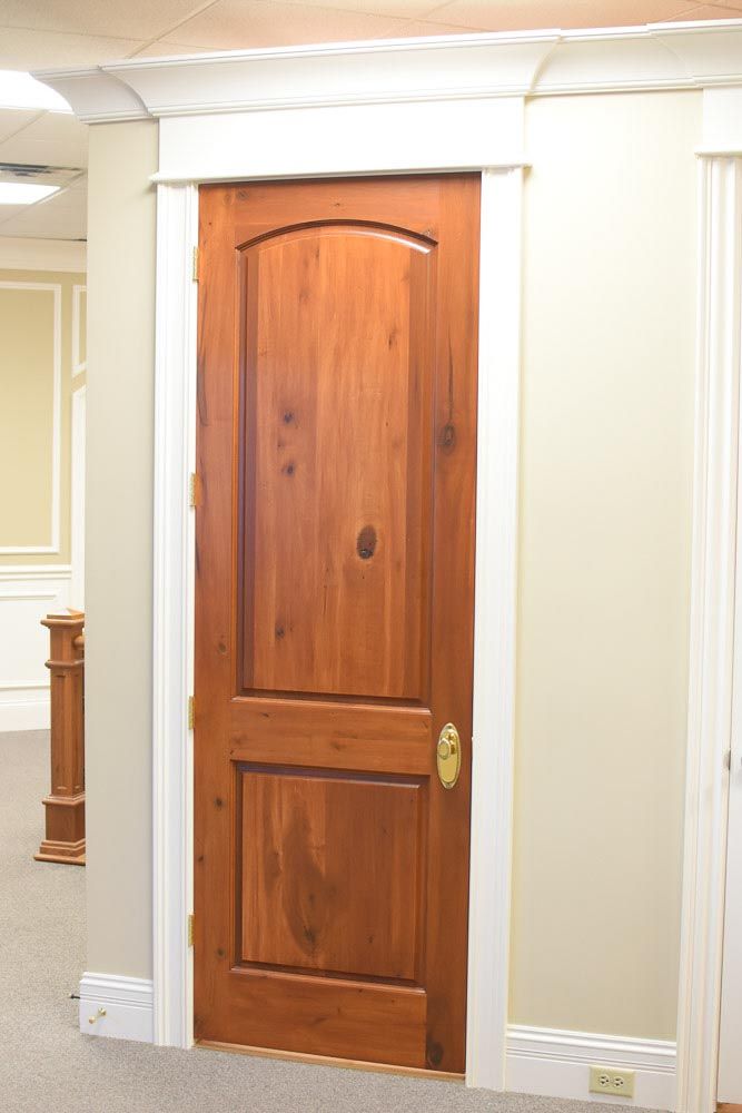 Wooden door with arched top and panel design, framed in white trim, set in a beige wall.