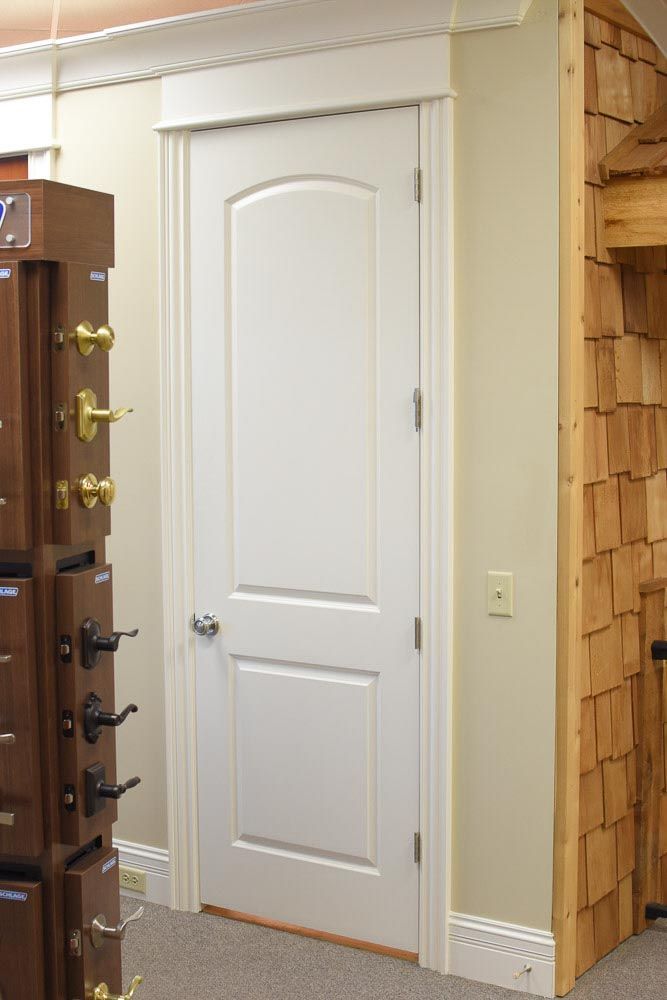 White two-panel door with arched top. White trim, beige wall, and wooden door hardware display.