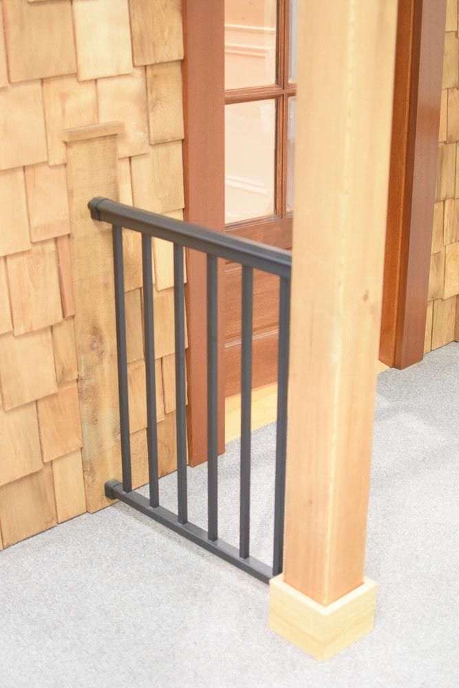 Black railing in front of a wooden door. Wooden pillar to the right. Wood shake siding.