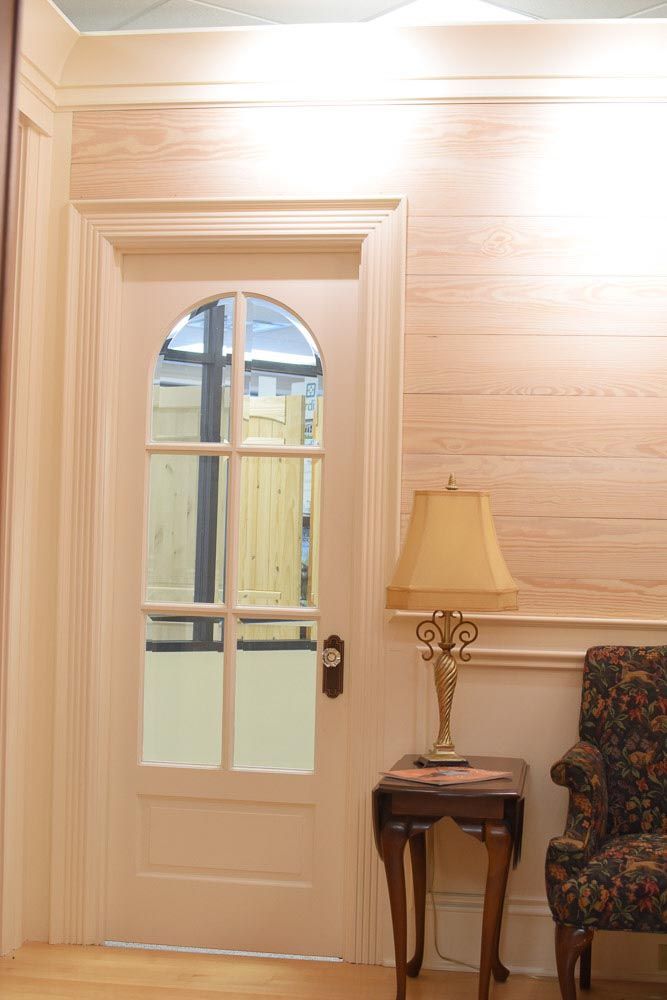 Doorway with arched window, table with lamp, and patterned armchair next to a wall with paneling and wood-grain texture.