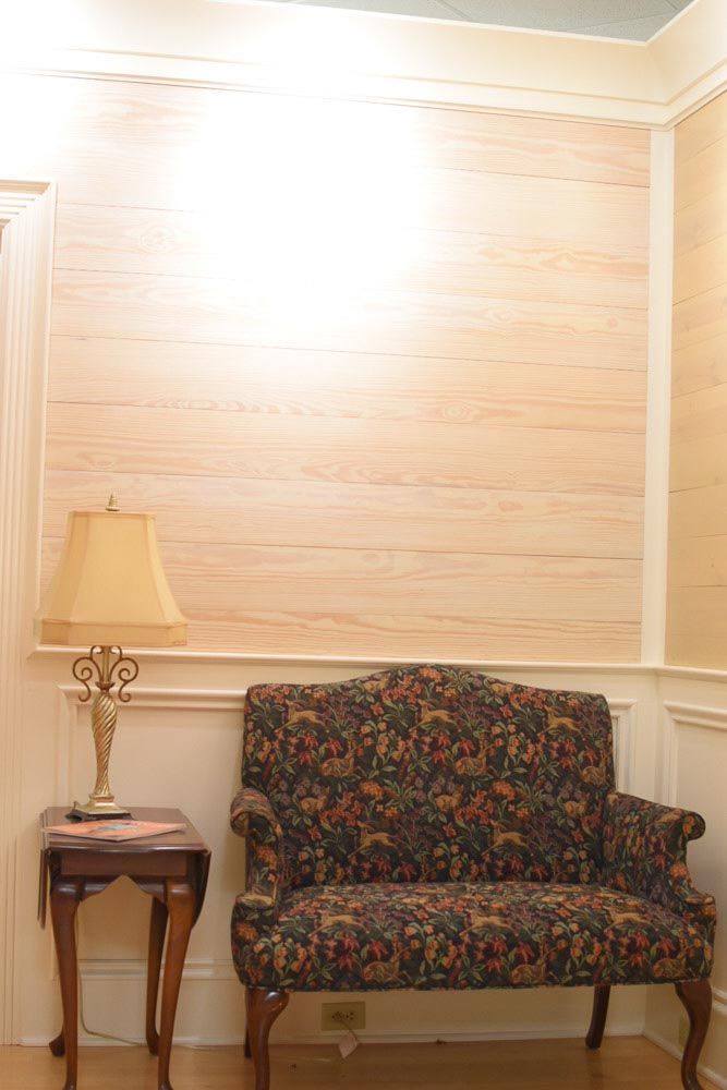 A small floral-patterned settee, lamp, and side table against a wood-paneled wall.