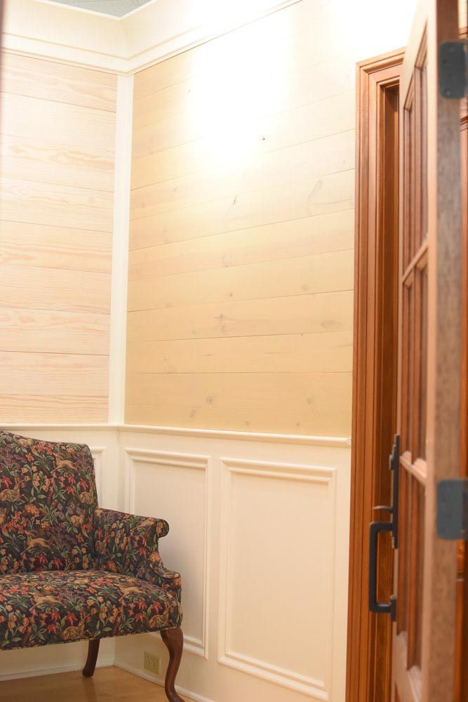 Upholstered chair in a room with wood panel walls, open door on the right.