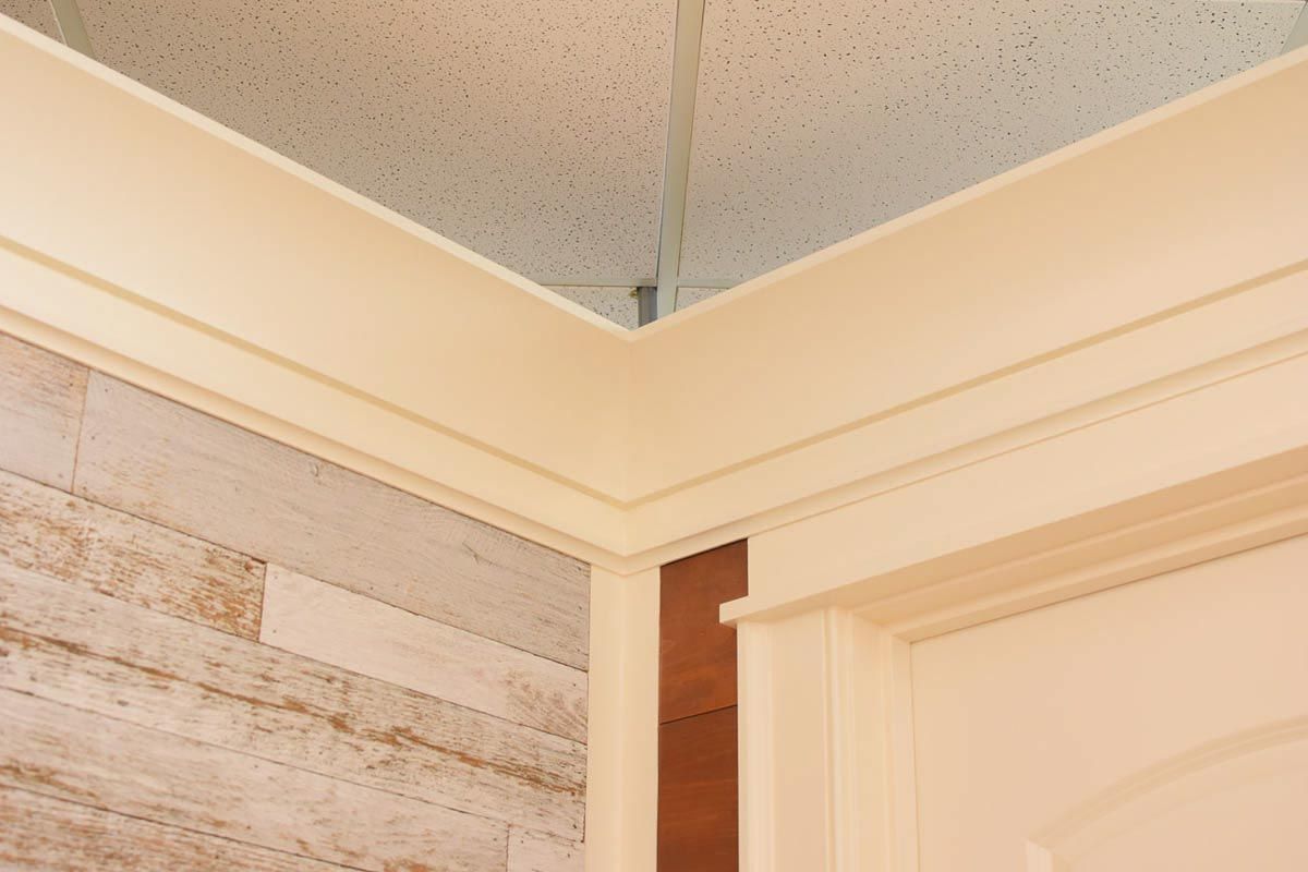 Corner of a room with white crown molding, a light-colored wood-look wall, and a door frame.