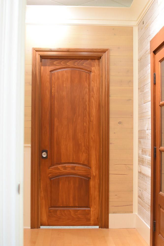 Wooden door with arched top and bottom panels in a hallway.
