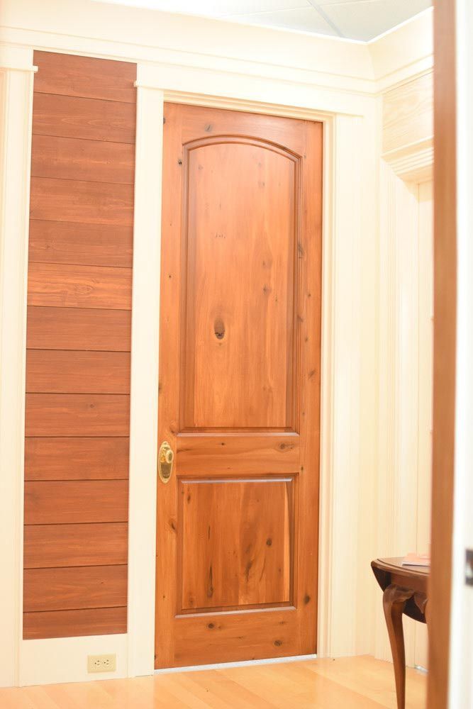 Wooden door with arched top and paneling, flanked by wood-paneled wall and entryway.