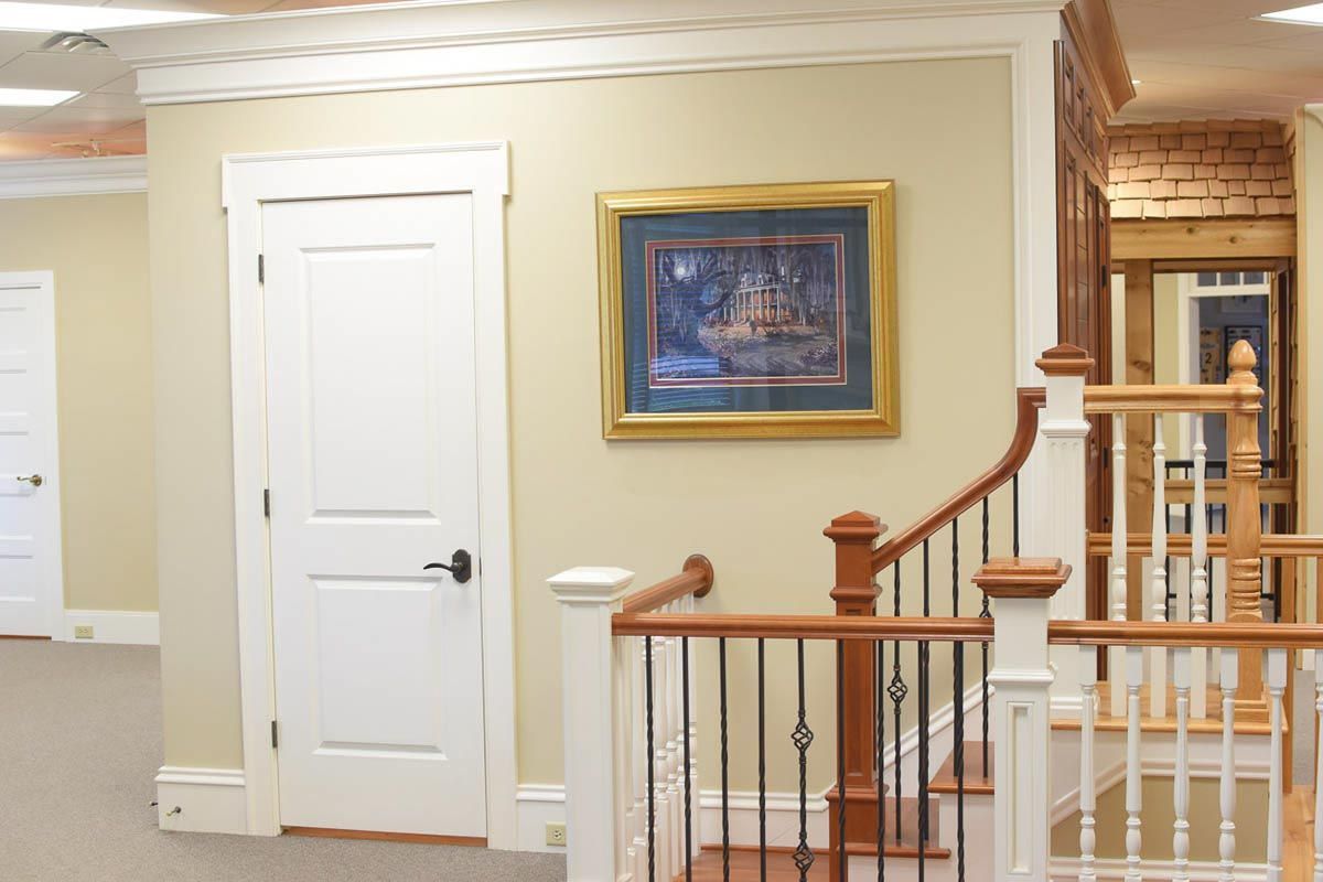 Hallway with staircase, closed white door, painting, beige walls, and wood banister.